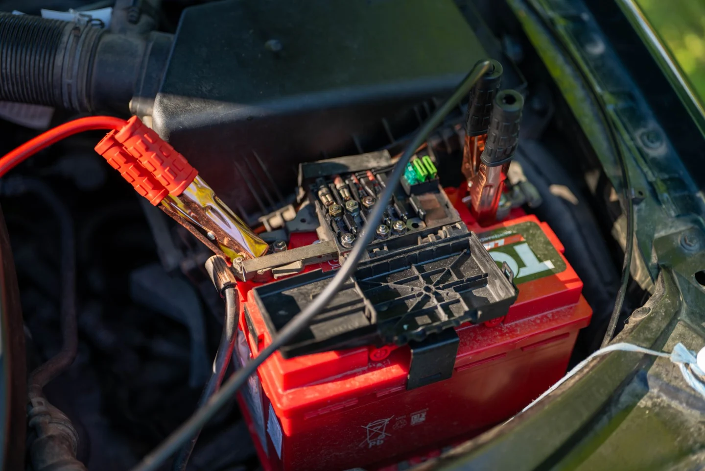 Red jumper cables connected to a car battery for a jump start